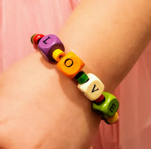 Load image into Gallery viewer, Our young ladies deserve all of the LOVE we can give them! This fun colored wood beaded bracelet has cube beads stamped with LOVE, individually. The LOVE beads are surrounded by colorful tube shaped beads and is completed with beautifully colored round beads.   The bracelets are made of stretch wire and come in sizes 6&quot; &amp; 6-1/2&quot;. If you would like a different size, please contact us.  *** Please note that the colors are random with regards to all of the bead types. ***
