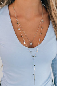  Layered silver necklace. One layer has a single charm. The other layer is contains star charms and beads with dark green tones. The full length is 17.5".